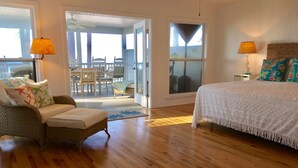 Une chambre avec un grand lit, un fauteuil en osier et une vue sur l’extérieur.