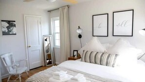 A bedroom with a bed, a chair, a mirror, and framed artwork on the wall. - Del Ray Designer Home walk to Shops, Cafes, Fun (Alexandria)