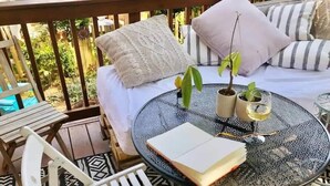 A cozy outdoor seating area with a round glass table, a white chair, and a cushioned bench. - Del Ray Designer Home walk to Shops, Cafes, Fun (Alexandria)
