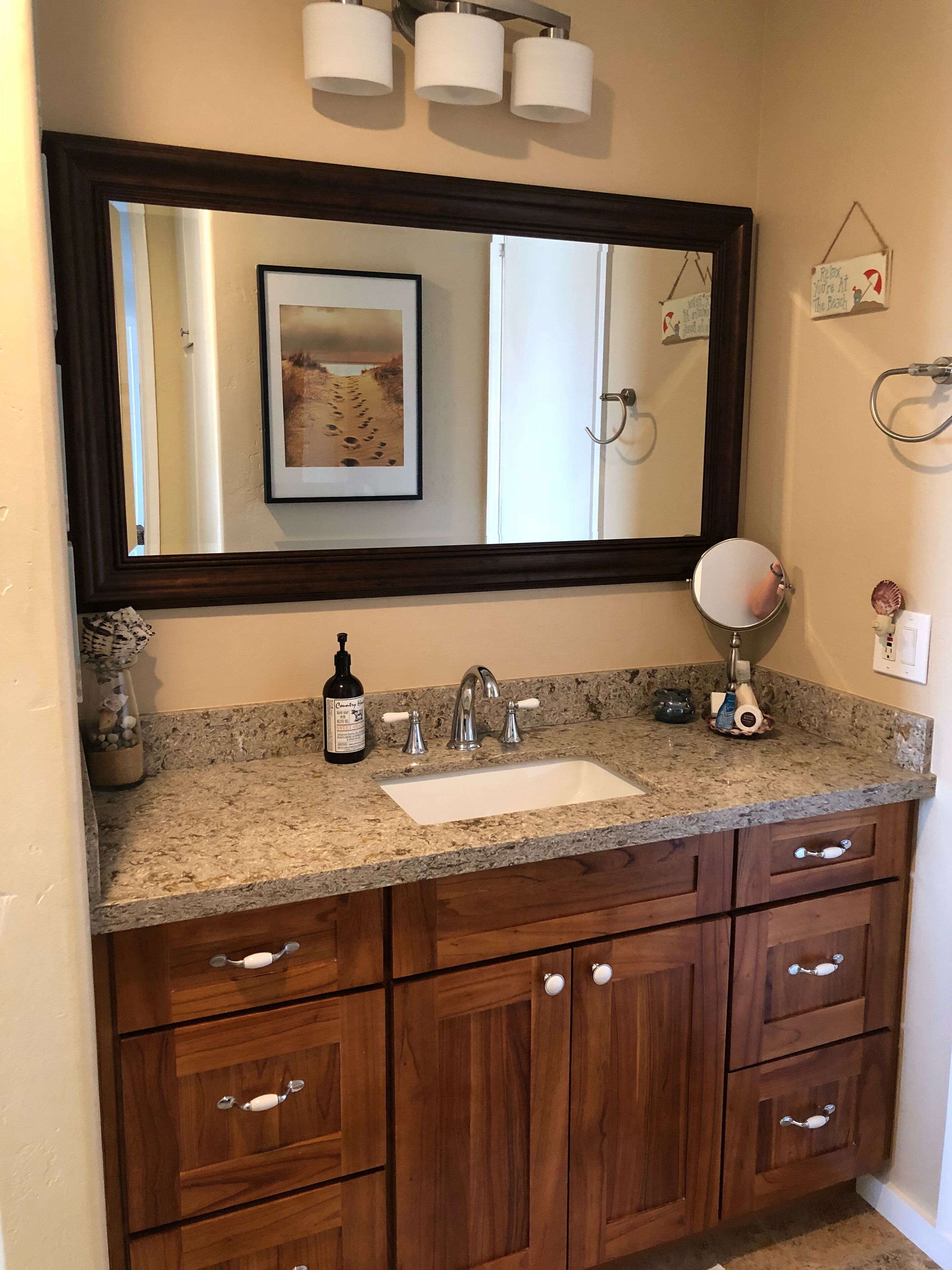 Une salle de bain avec un comptoir en granit, un lavabo blanc, un grand miroir et des armoires en bois.