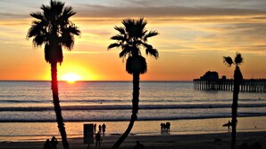 Una playa al atardecer, con palmeras y un muelle al fondo.