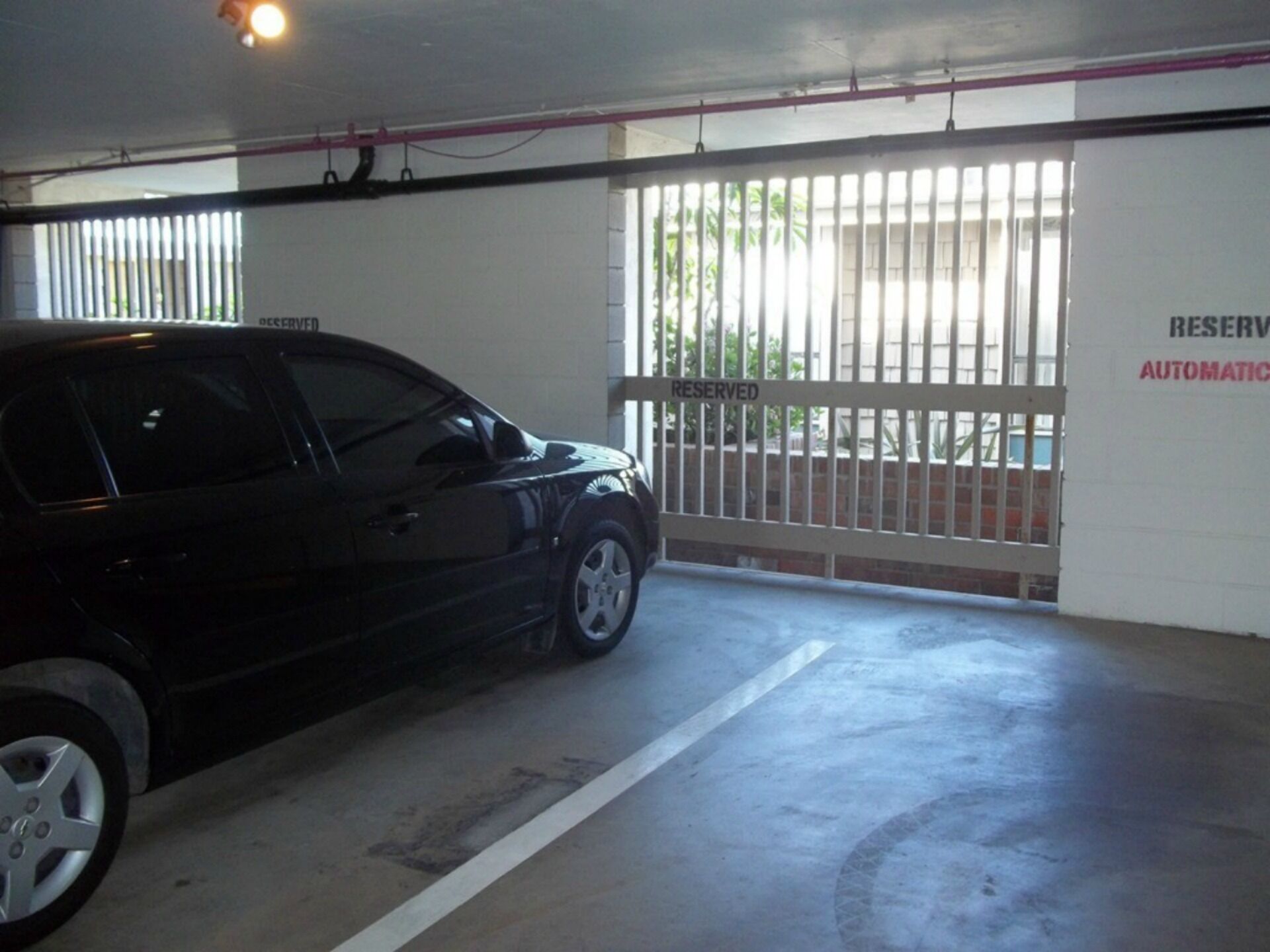 Un estacionamiento con un coche negro aparcado cerca de una entrada con puerta.