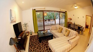 A living room with a sofa, a coffee table, a TV, and a dining area with a table and chairs. - 2 Bedroom Apartment In Quiet Secure Residential Complex Surrounded By Nature (Akumal)