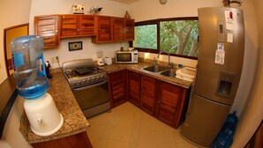 A kitchen with granite countertops, wooden cabinets, a stainless steel refrigerator, a microwave, a stove, and a sink. - 2 Bedroom Apartment In Quiet Secure Residential Complex Surrounded By Nature (Akumal)