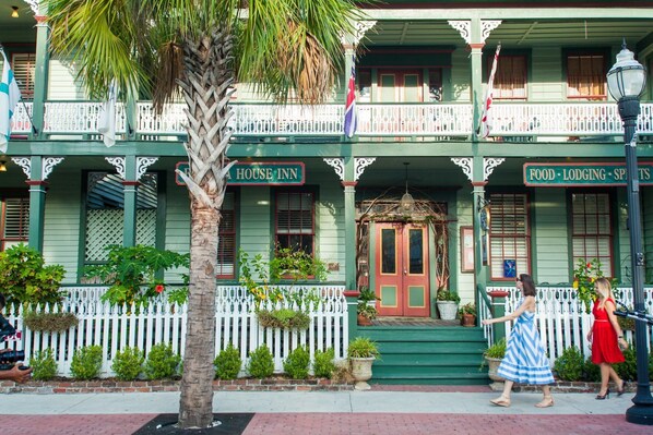 A two-story building with a balcony, a sign reading "Food - Lodging - Sports", and a palm tree in the foreground.