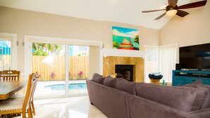 A living room with a sofa, a dining table with chairs, a fireplace, a TV, and a ceiling fan. - Relax by the sea! 3-Bedroom Delray Beach Home near Atlantic Ave (Delray Beach)