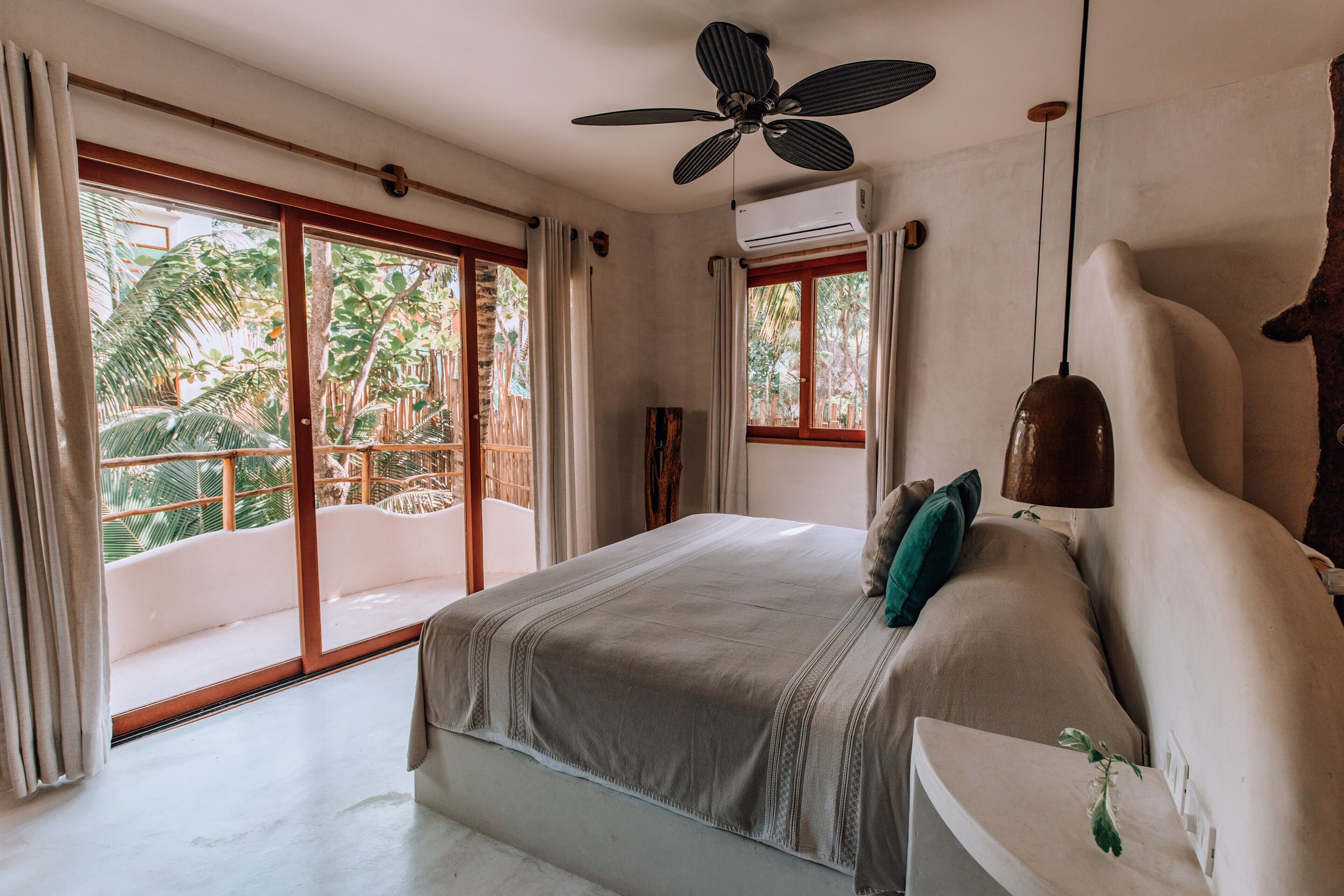 Une chambre dotée d’un grand lit, d’un ventilateur de plafond et offrant une vue sur un jardin tropical grâce à ses portes-fenêtres coulissantes.