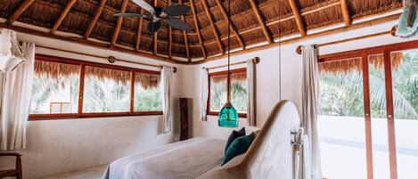 A bedroom with a bed, a ceiling fan, and large windows with curtains.