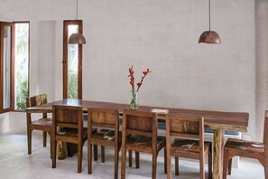 Un espace repas comprenant une longue table en bois, six chaises et deux lampes suspendues.