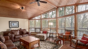 A spacious living room with a wooden ceiling, large windows, and a variety of seating including a sofa, chairs, and a table.