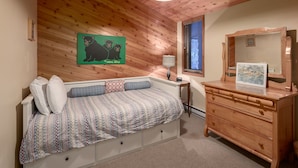 A cozy room with a wooden ceiling, a bed with patterned bedding, a dresser with a mirror, and a framed picture on the dresser.