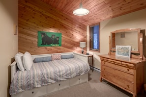Una habitación acogedora con techo de madera, una cama con ropa de cama estampada, un aparador con espejo y un cuadro en el aparador.