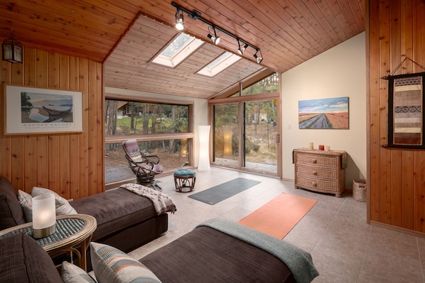 Una habitación acogedora con techo de madera, ventanas grandes, un sofá, una silla, una mesita y un aparador.