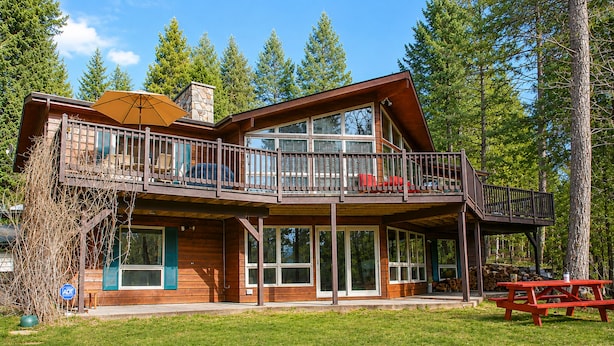 A two-story lodge with a balcony, large windows, and a picnic table.