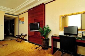 A hotel room with a wooden floor, a desk with a computer, a TV, and a large mirror. - King Sa Hotel (Shishi)