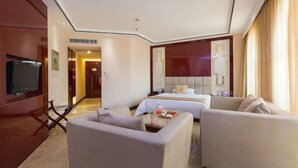 Habitación de hotel con una cama, dos sofás, un televisor y una mesita con objetos encima.
