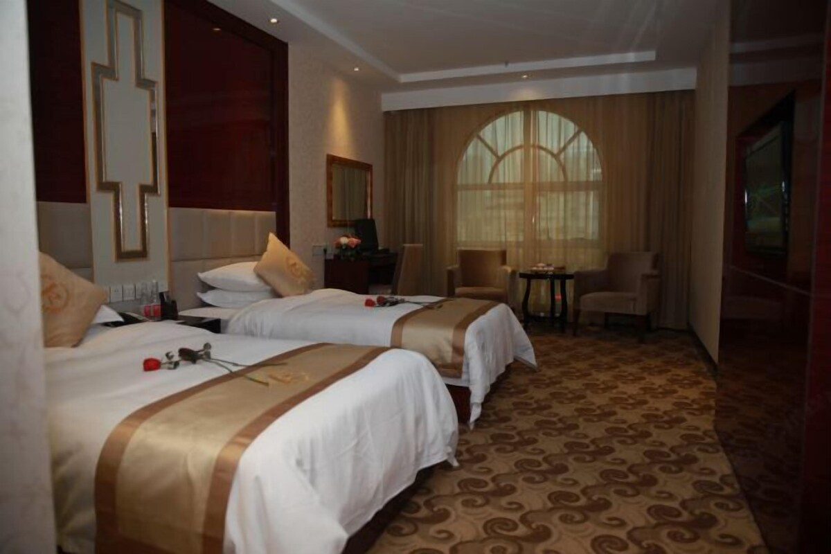 A hotel room with two beds, a desk, a chair, and a large window.
