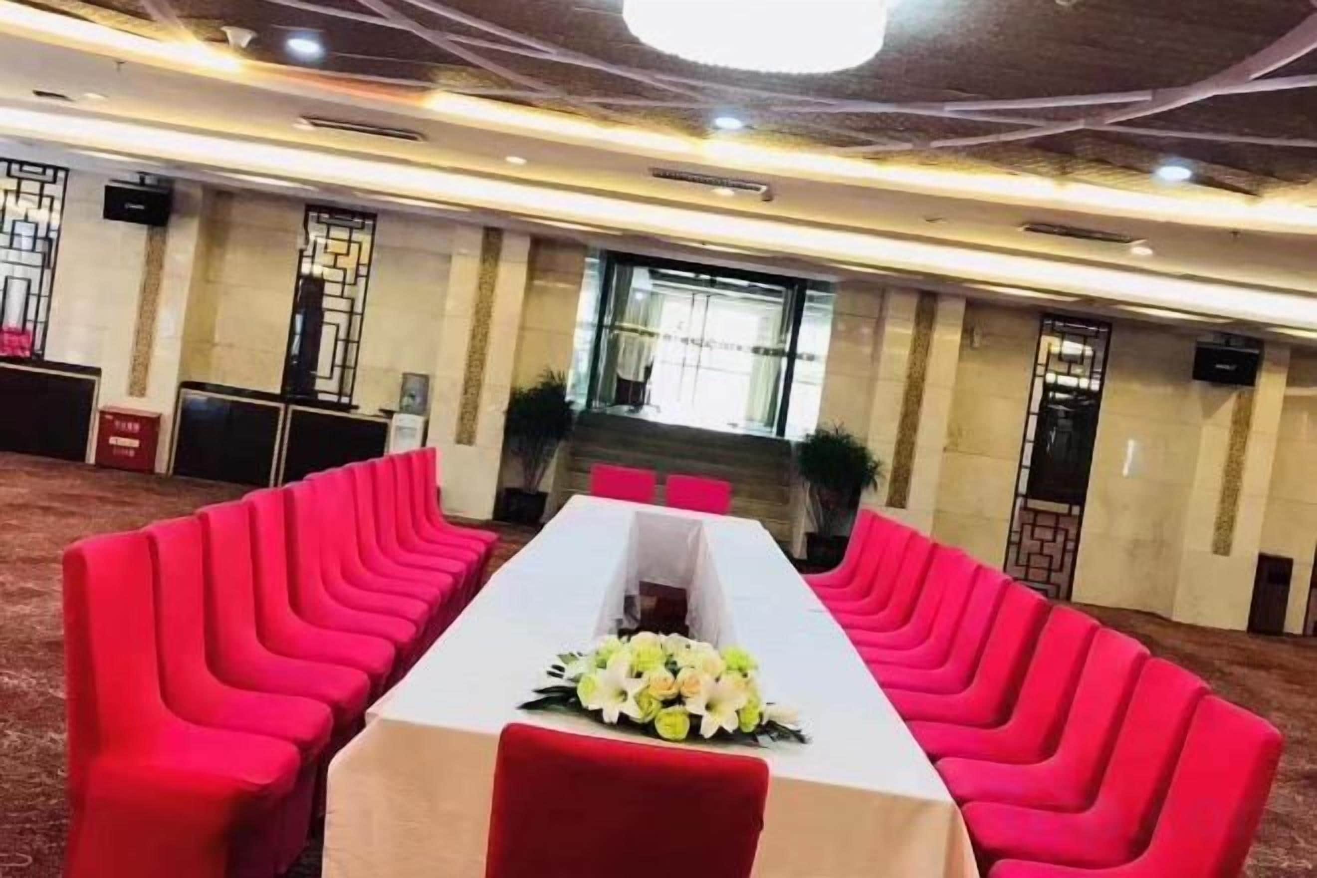 Ein Konferenzraum mit einem langen Tisch, roten Stühlen und einer Blumenarragemement.
