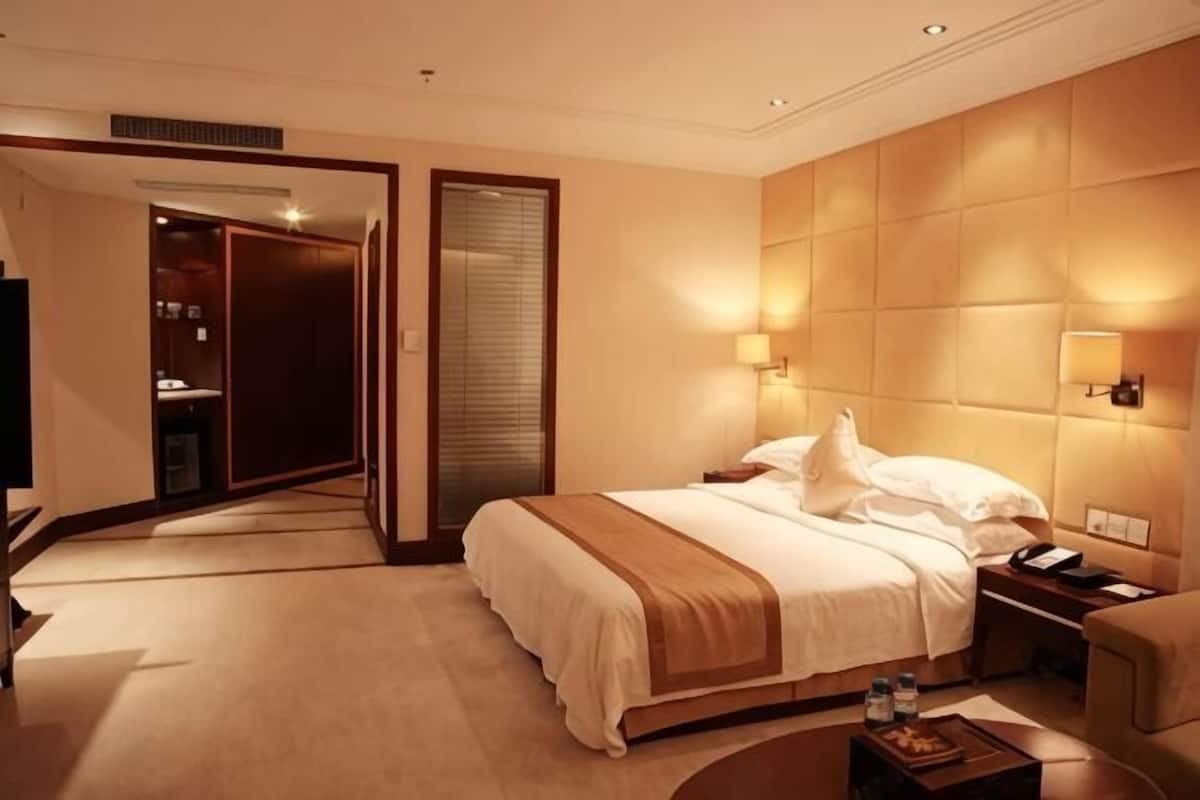 A hotel room with a bed, bedside table, lamp, and a door leading to a bathroom.