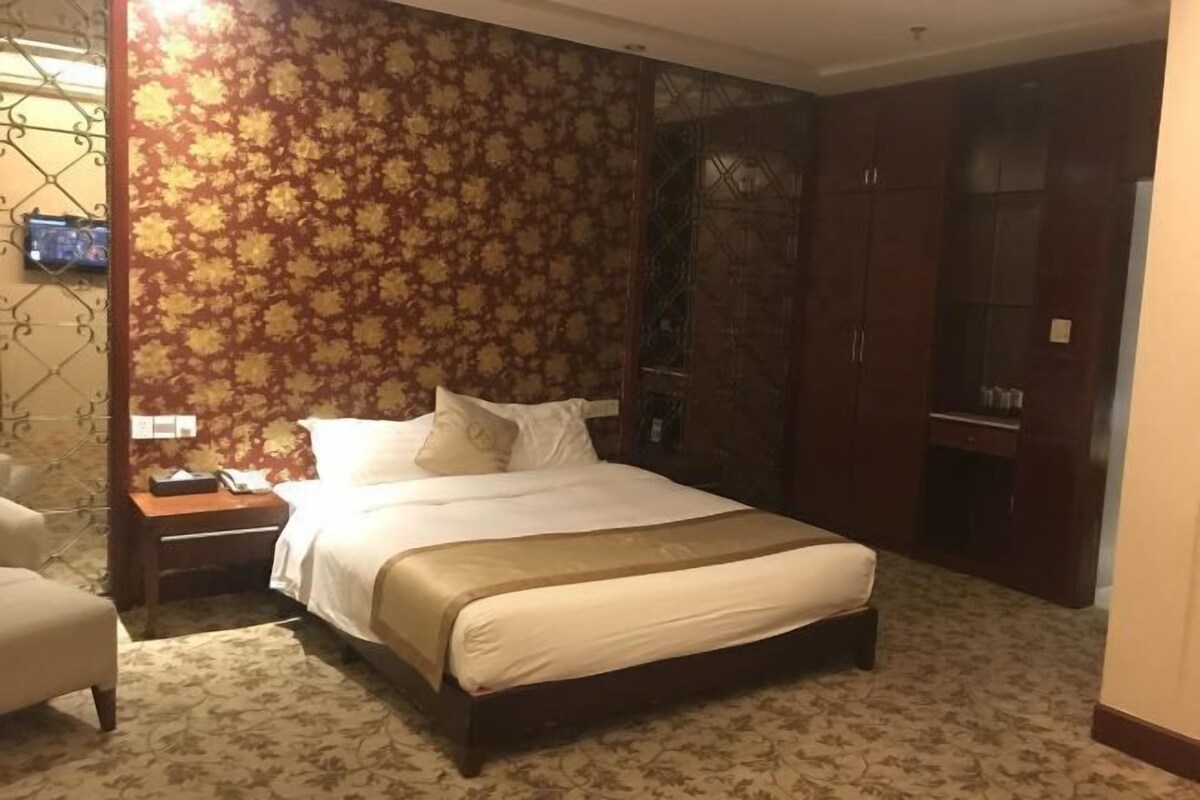A hotel room with a large bed, a wooden wardrobe, and a patterned carpet.