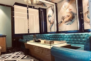 A room with a blue upholstered bench, a table with a glass top, and a large abstract painting on the wall. - King Sa Hotel (Shishi)