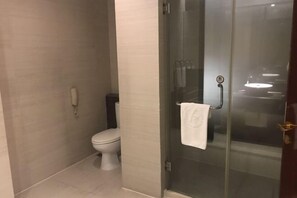 A modern bathroom with a toilet, a glass shower enclosure, and a telephone. - King Sa Hotel (Shishi)