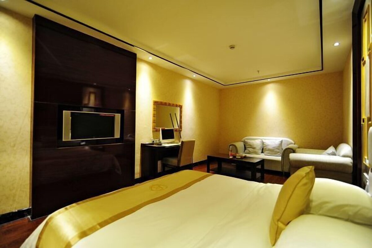 A hotel room with a bed, a desk, a chair, a sofa, and a television.
