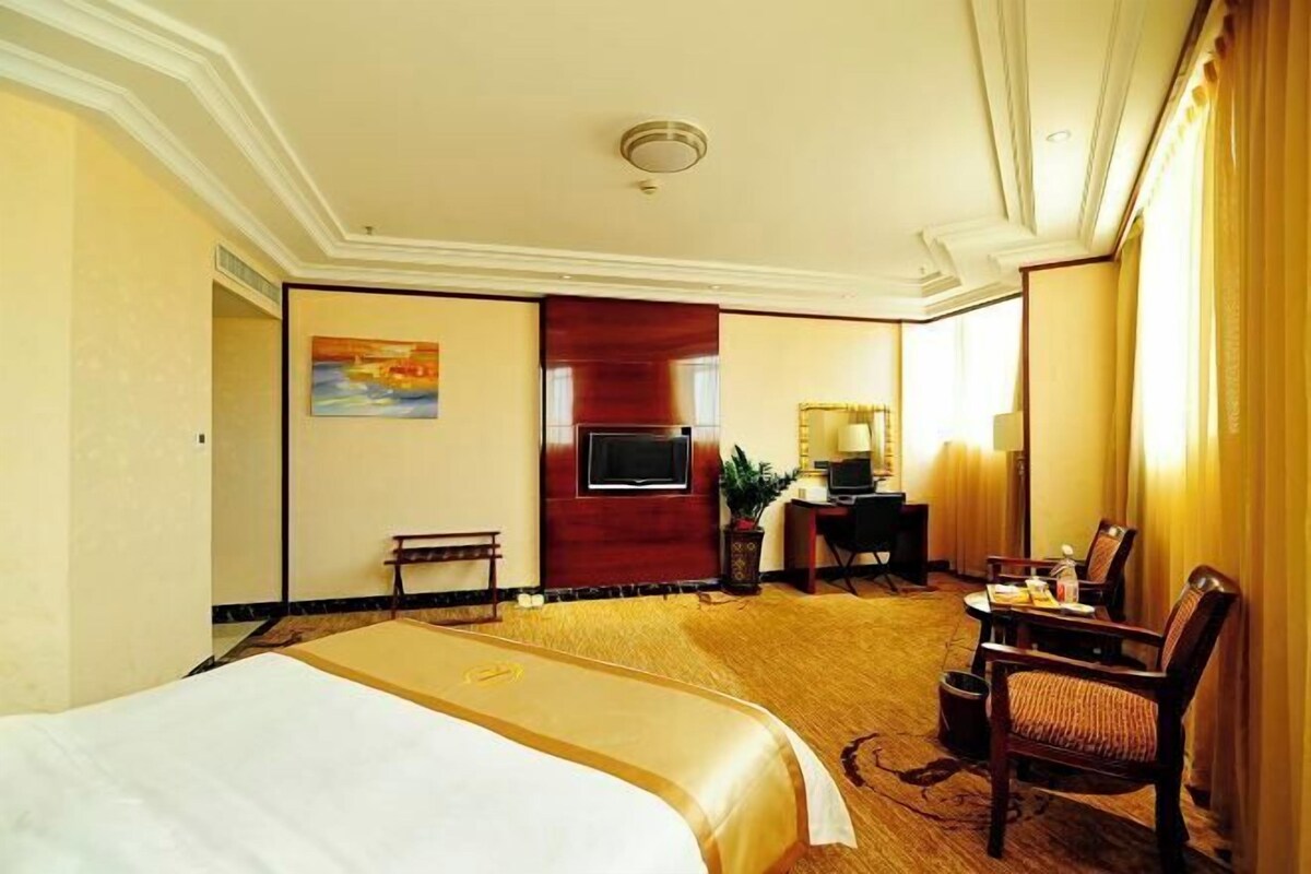 A hotel room with a large bed, a desk with a computer, a TV, and a chair.