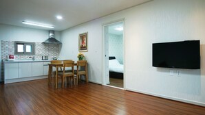A compact living space with a kitchenette, a dining area with wooden chairs, a bed in the adjacent room, and a mounted TV. - Jeju J Pension (Seogwipo)
