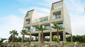 A multi-story building with a modern architectural design, featuring balconies and large windows. - Jeju J Pension (Seogwipo)