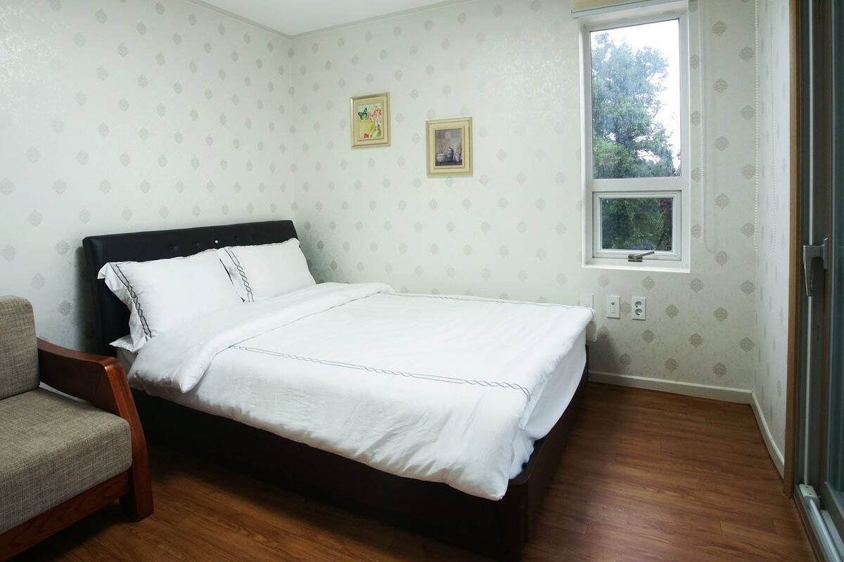 A bedroom with a bed, a sofa, a window, and a door.