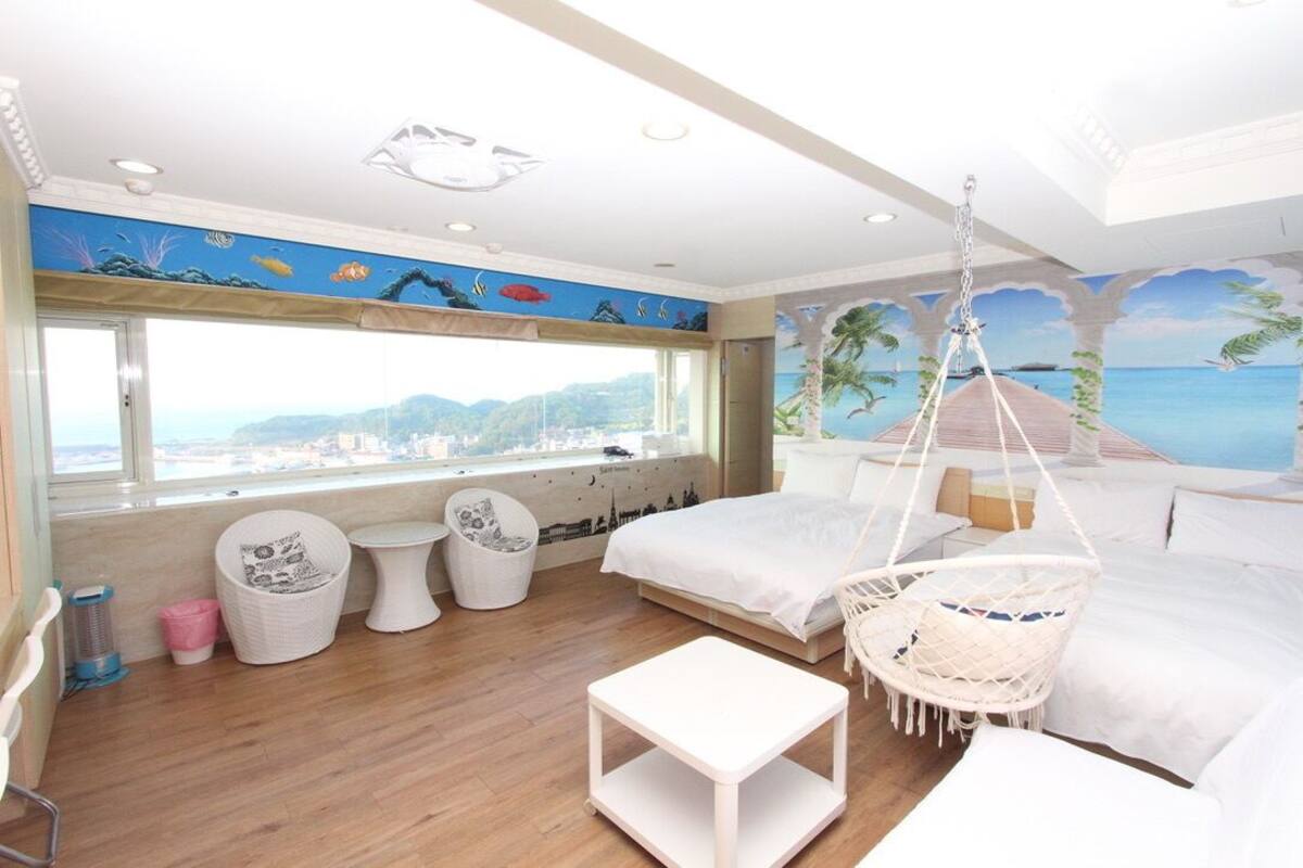 A bedroom with a large window, two beds, a hanging chair, and a small table.