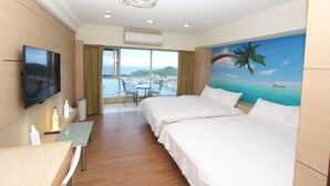 A hotel room with two beds, a TV, a desk with a chair, and a view of the sea and a palm tree through large windows. - HF Keelung 61 (Keelung)