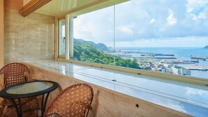 A balcony with wicker chairs and a table, overlooking a coastal cityscape with greenery and water. - HF Keelung 61 (Keelung)