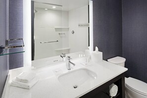 Ein modernes Badezimmer mit Waschbecken in Weiß, einem großen Spiegel, einer Duschkabine aus Glas und einer weißen Toilette.