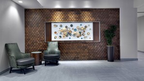Un hall d’entrée moderne avec un mur orné d’un motif géométrique, un grand élément décoratif mural, deux fauteuils, une table ronde et une plante en pot.