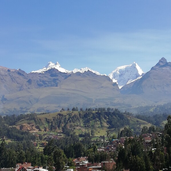A mountainous landscape with snow-capped peaks, a valley with scattered houses, and a clear blue sky. - Artesonraju Hostel Huaraz (Huaraz)