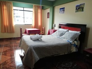A hotel room with a bed, a window with curtains, a small table with a red tablecloth, and a chair. - Artesonraju Hostel Huaraz (Huaraz)