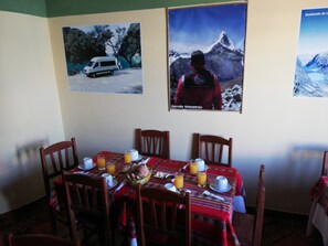 A dining area with a table set for four, featuring a red tablecloth, wooden chairs, and a basket with a baby. - Artesonraju Hostel Huaraz (Huaraz)