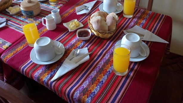 A breakfast table set with cups, plates, bread, and orange juice.