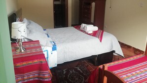 A hotel room with a bed, a desk with a lamp, a television on the wall, and a wardrobe.