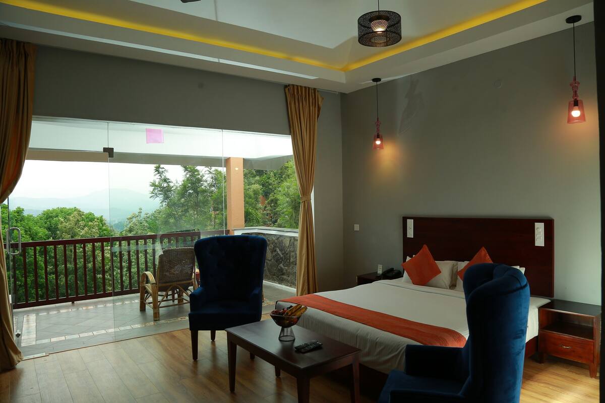 A hotel room with a large bed, a balcony with a view, a wooden table, and two chairs.
