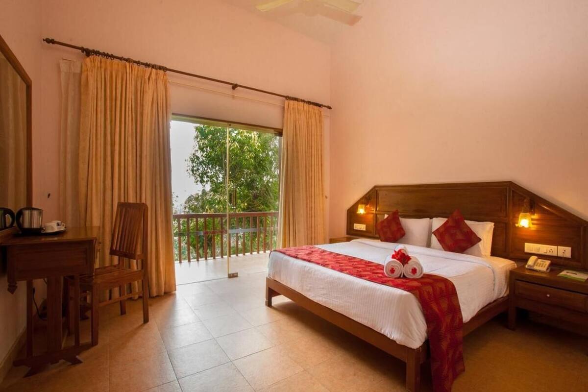 A hotel room with a bed, a desk, a chair, a nightstand, and a balcony with curtains.