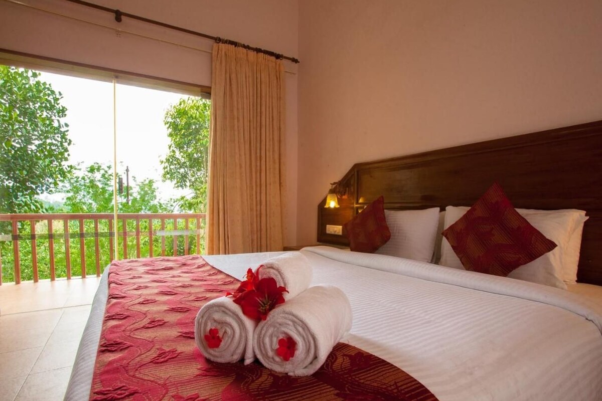 A hotel room with a large bed, a balcony with a view of trees, and a wooden headboard.