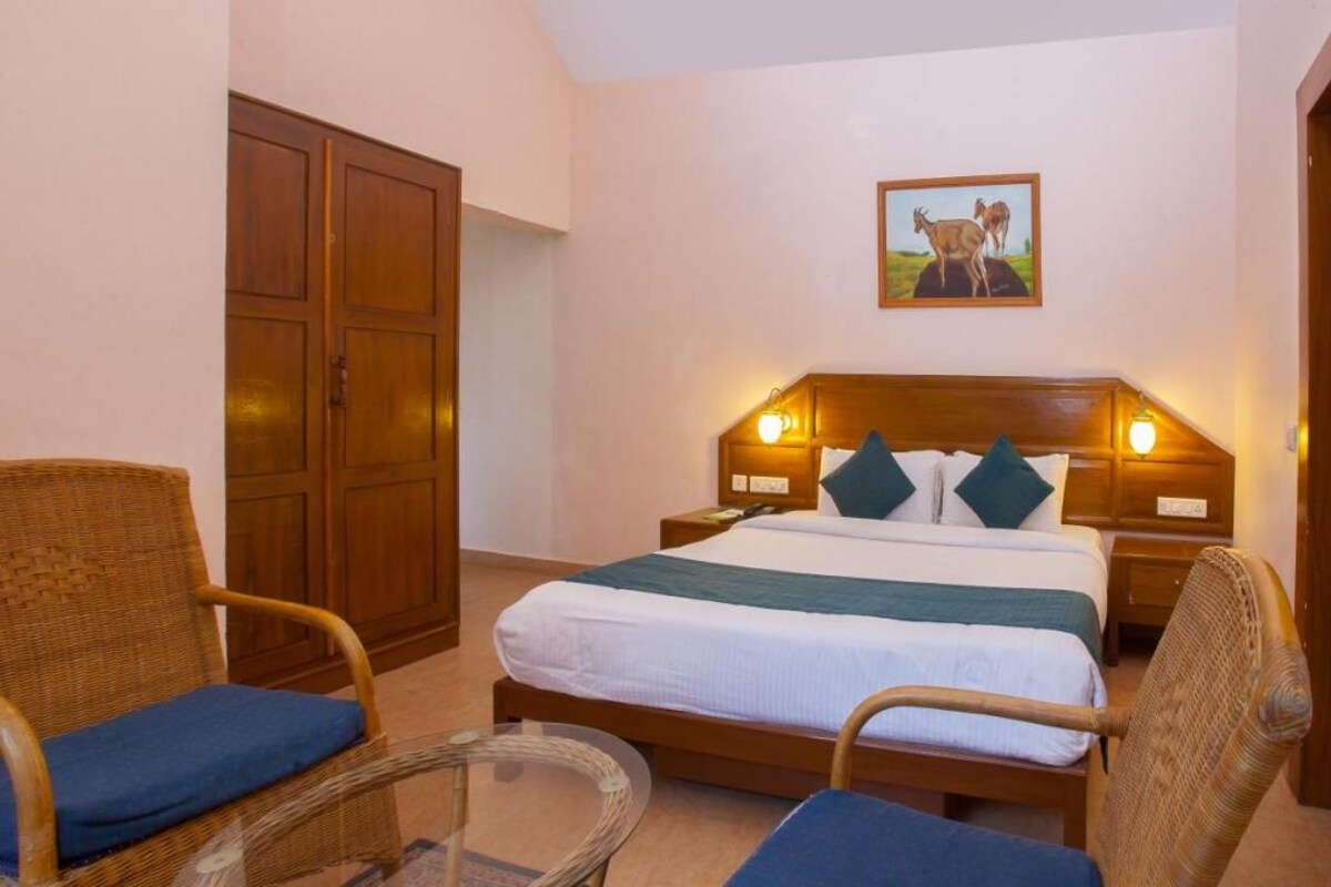 Un dormitorio con una cama, dos sillones de mimbre, un armario de madera y un cuadro en la pared.