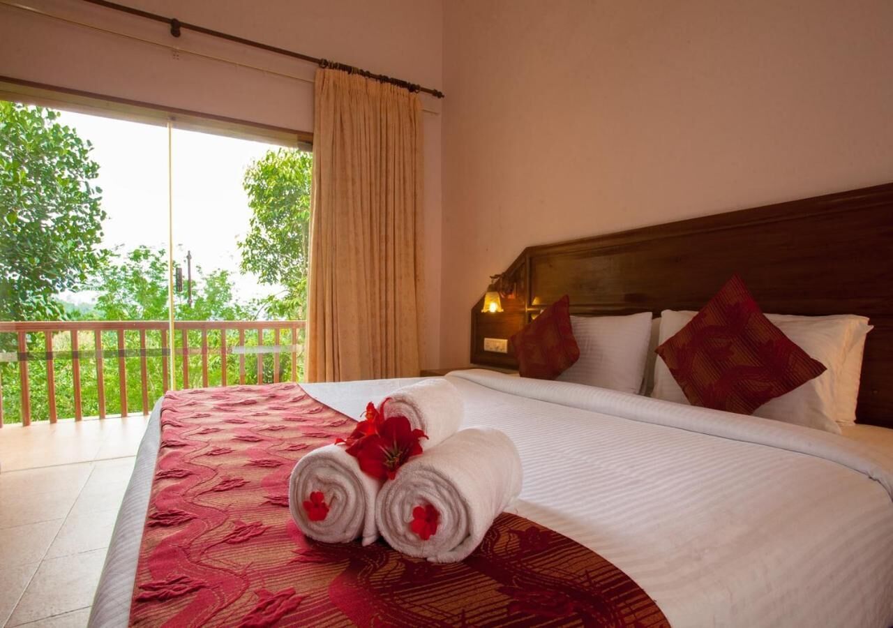 Een hotelkamer met een groot bed, een balkon met uitzicht op bomen, en een houten hoofdbord.