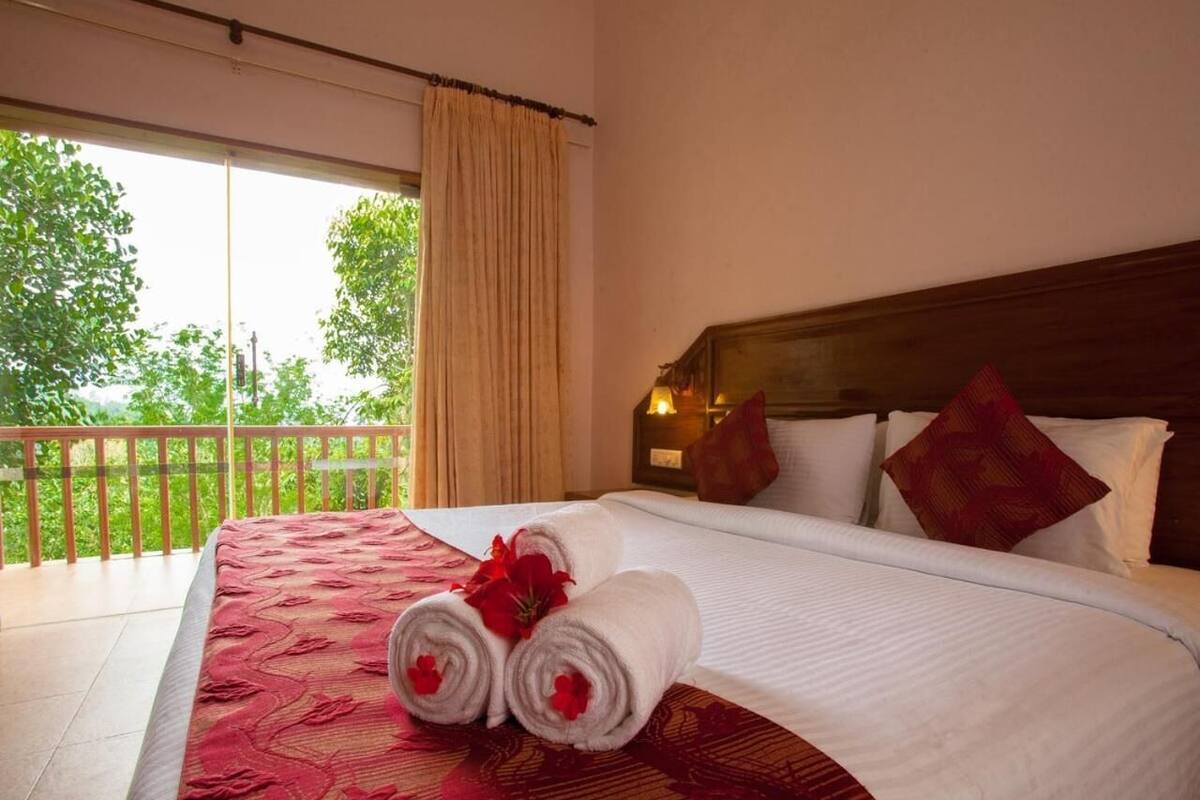 A hotel room with a large bed, a balcony with a view of trees, and a wooden headboard.