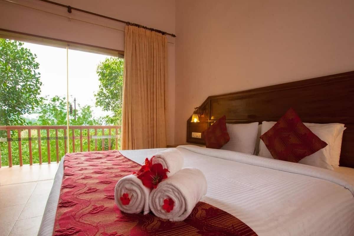 Habitación de hotel con una cama grande, un balcón con vistas a árboles y un cabecero de madera.