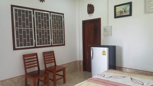 A room with two wooden chairs, a small refrigerator, a door, and a wall-mounted picture. - Pings Farmstay (Somboon)