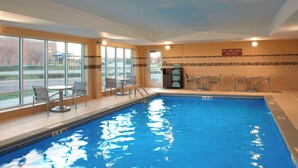 A swimming pool with clear blue water, surrounded by windows and chairs. - TownePlace Suites by Marriott Grand Rapids Airport (Grand Rapids)